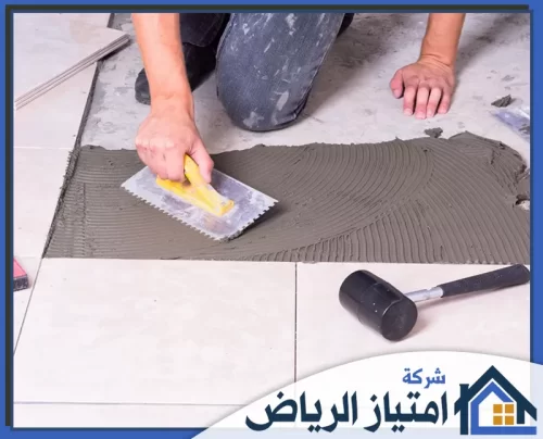 معلم بلاط بالرياض 0506986916 شركة امتياز الرياض لقطة قريبة لعملية تبليط أرضية، تظهر توزيع اللاصق بانتظام وأدوات العمل اليدوية.