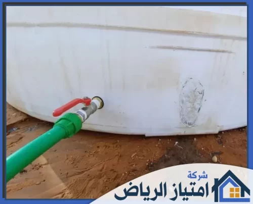تصليح خزانات فيبر جلاس بالرياض 0506986916 شركة امتياز الرياض منظر مقرب لخرطوم أخضر وصنبور على خزان مياه أبيض، مع وجود رقعة إصلاح في الخلفية.