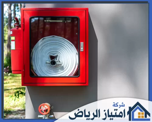 معالجة تسربات الحريق بالرياض 0506986916 شركة امتياز الرياض خزانة إطفاء حمراء تضم خرطوم حريق ملفوفًا بعناية، بجانبها طفاية جاهزة، لضمان استجابة سريعة وفعالة في الطوارئ.
