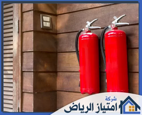 صيانة خطوط الحريق بالرياض 0506986916 شركة امتياز الرياض طَفايتا حريق بلون أحمر زاهٍ معلقتان على جدار خشبي بني، تعكسان أعلى معايير السلامة والأمان في المنشآت الحديثة.